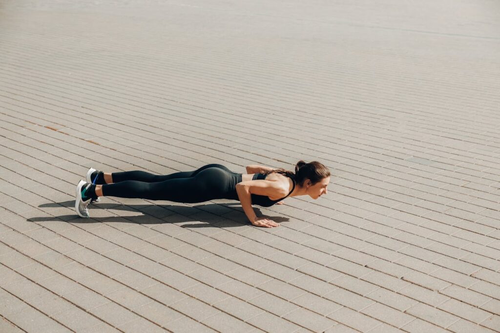 Fit woman in activewear performing push-ups outdoors on a sunny day.