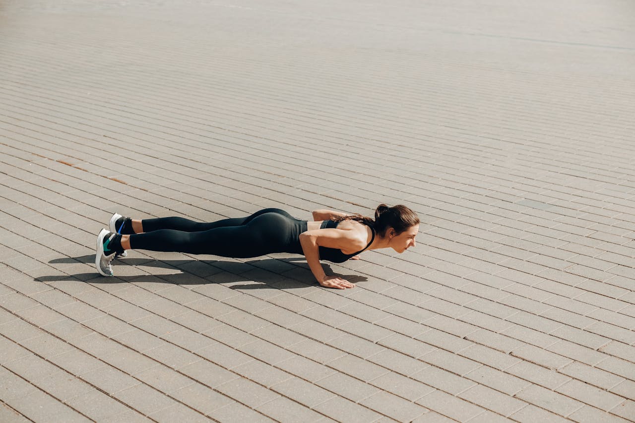 Fit woman in activewear performing push-ups outdoors on a sunny day.